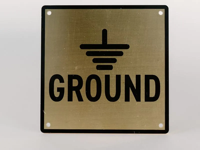 A brass equipment ground plate with the earth-ground symbol and black-filled engraving