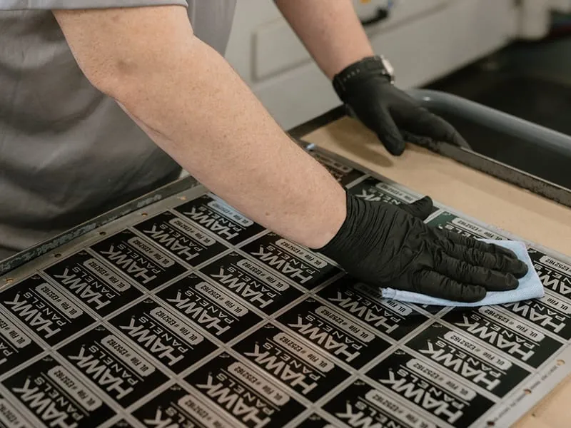 A craftsman wiping down a freshly marked sheet of black anodized plates