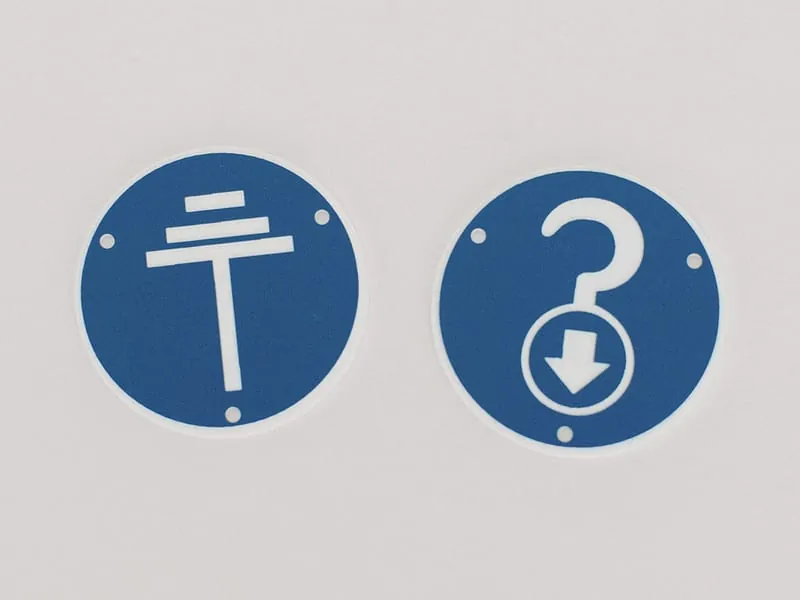 Two blue plastic pictogram discs marking equipment functions