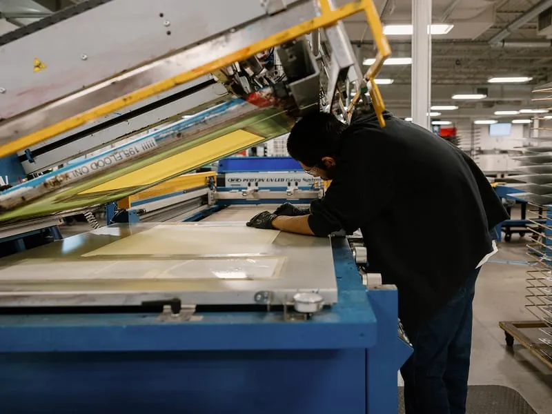 An operator aligning a metal sheet on the press bed beneath the raised screen