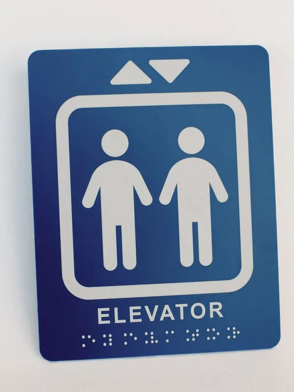 A blue ADA elevator sign with pictogram, lettering, and braille